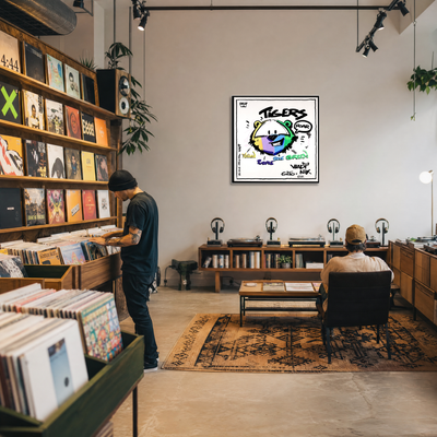 Gito Fine Art Print - Art Vladi Vl Comics - Tigers
A framed wall art print featuring a colorful cartoon tiger face with the word 'TIGERS' and small text, displayed in a modern record store interior with vinyl records, shelves, headphones, and two people present.