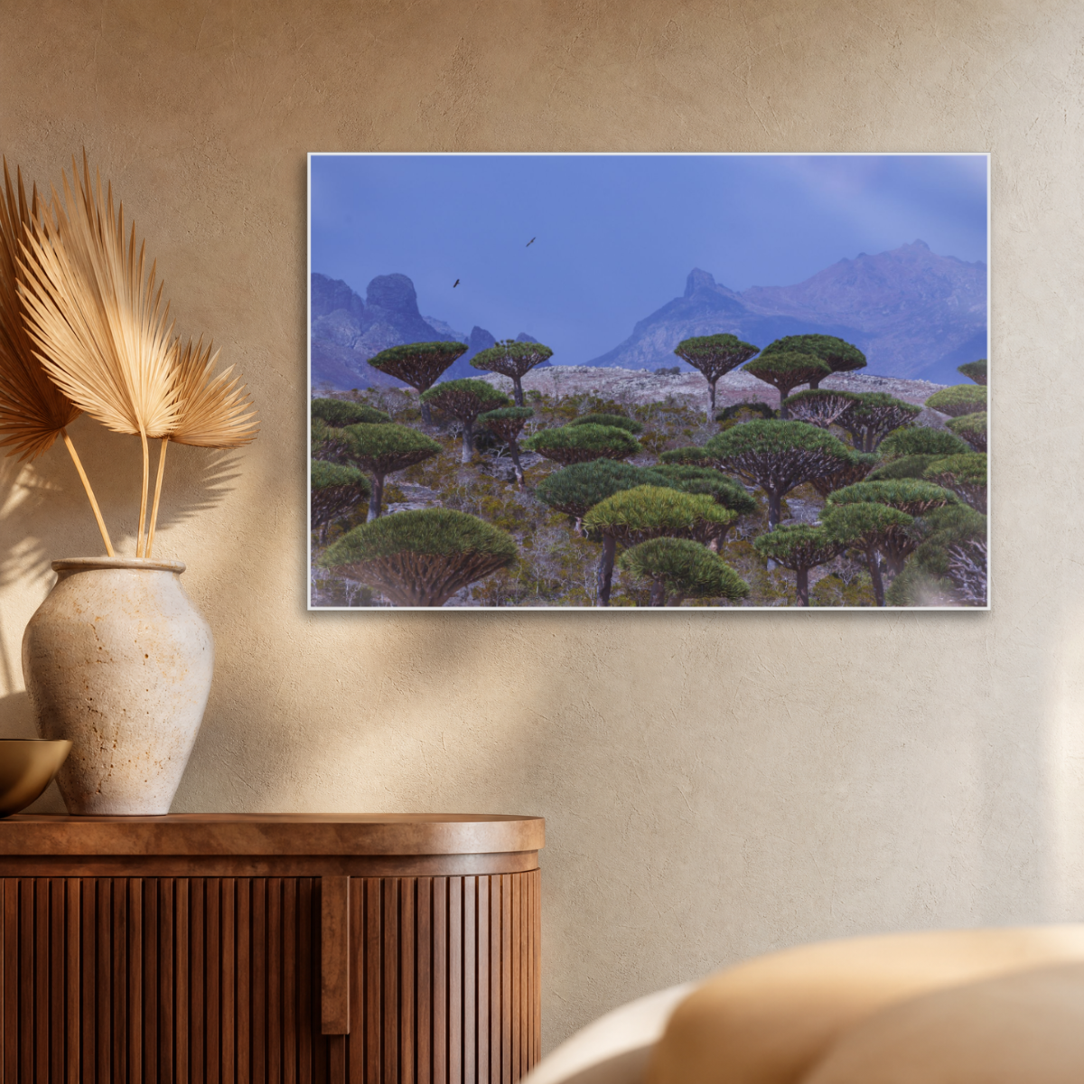Gito.Art - Exclusive Art Print - Photography by Delyan Markov
A framed landscape art print depicting green dragon blood trees in a desert landscape under a blue sky, displayed on a beige wall above a wooden sideboard with a vase.