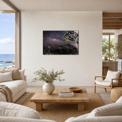 Gito.Art - Exclusive Art Print - Photography by Delyan Markov
A framed wall art print depicting a night sky with the Milky Way and silhouetted trees is displayed above a wooden coffee table in a bright, modern living room with white sofas and a view of the ocean.