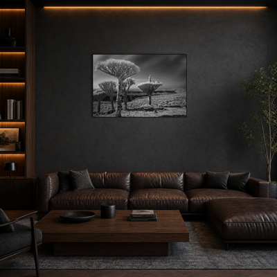 Gito.Art - Exclusive Art Print - Photography by Delyan Markov
A black and white landscape wall art print depicting quiver trees is displayed on a dark textured wall above a brown leather sectional sofa in a modern living room setting.