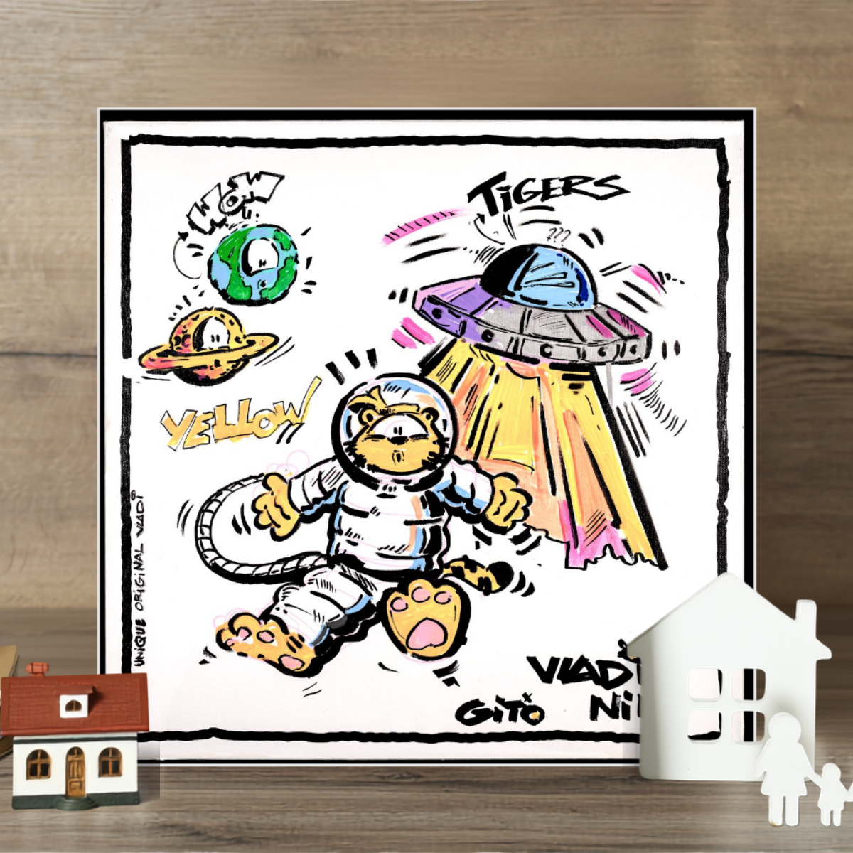 Gito Fine Art Print - Art Vladi Vl Comics - Tigers
A square framed art print featuring a cartoon astronaut tiger, a UFO, planets, and playful text, displayed on a wooden surface with small decorative houses in the foreground.